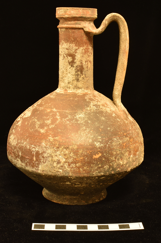 Body bulbous in upper 2/3 with carination to almost straight-sided lower 1/3, low pedestal base; tall cylindrical neck with sharp horizontal ridge at top, vertical rim; broad handle deeply concave on exterior a central rib, from shoulder to raised ridge at top of neck.  Shallow incisions at top and base of rim and defining shoulder: two close to base of neck, two slightly lower, and two more just above level of handle.  Coated all over exterior and on inside of rim with dark paint.