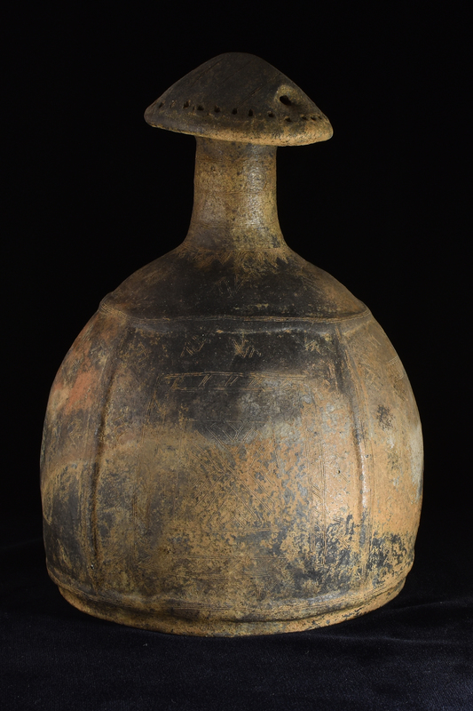 Imitation in clay of bronze helmet.  Rounded body rising from top of which tall, very slightly tapering cylindrical neck w finial in form of gabled roof which perforated horizontally under gable and by row of small holes around circumference of edge.  Body below neck & just above base set off by horizontal rib above & below and space between ribs divided into 4 sections by single vertical raised ribs.  Surfaces & ribs decorated with fine incision: on neck concentric horizontal lines, on shoulder pendant triangles below which isolated multiple zigzag devices, within ribbed sections metopes decorated with geometric patterns & surrounded by border of multiple zigzag devices; widely spaced groups of incised lines running across roof. Burnished surface.