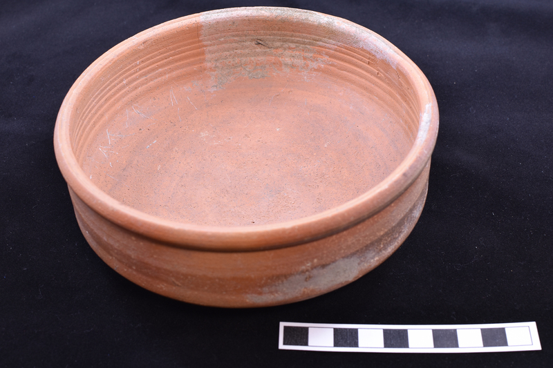 Low open bowl with straight sides and rolled rim, prominent wheel marks on interior walls; shallowly convex base with fine ribbing on outer half.  Painted stripe on exterior rim and just above base on exterior walls.