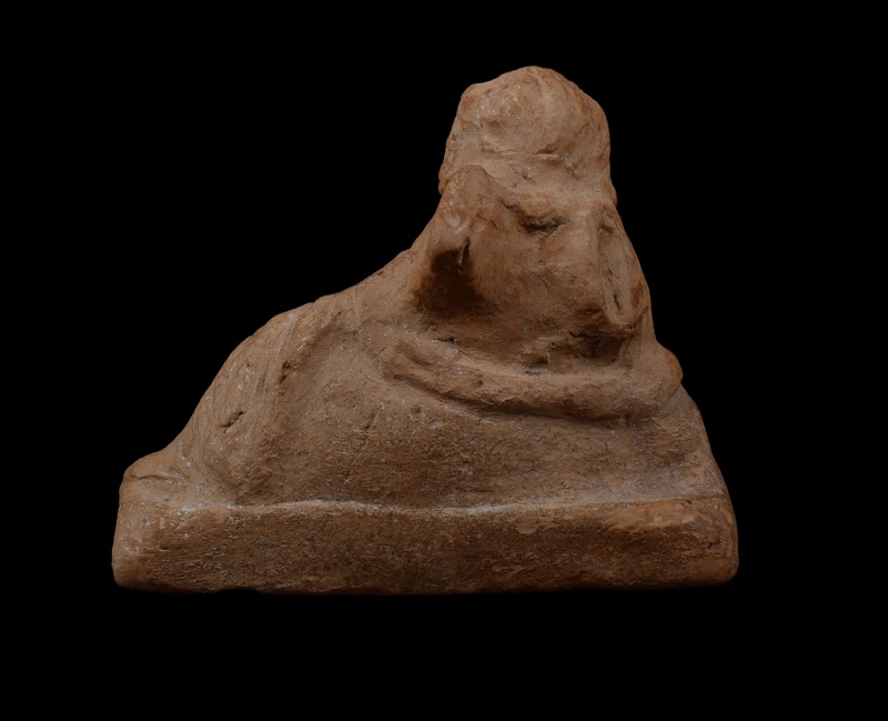On rectangular base chubby Eros reclining on right elbow with right hand on rabbit.  Round face with eyebrows, eyes, nostrils, mouth, and cleft in chin articulated by incision; wreath on head with hair articulated by incisions going from forehead down back of head on either side of wreath, with clumps of hair articulated by irregular incision falling on either side of head.  Left arm covered by drapery stretched out and resting on bent left leg; incised lines roughly articulating folds of drapery; some articulation of feathers of left wing.  Raised band runs around back of figure under back of wings, possibly meant as drapery.