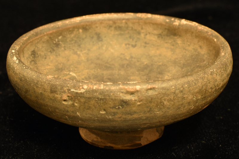 Bowl w shallowly convex sides rising fr low pedestal base, deeply conical on nippled underside, to rounded shoulder w fairly thick plain rim.  Incised line on lower body above base.  Coated all over int and most of ext w dark paint which ran onto underside of base.  Defects on exterior wall painted before firing.