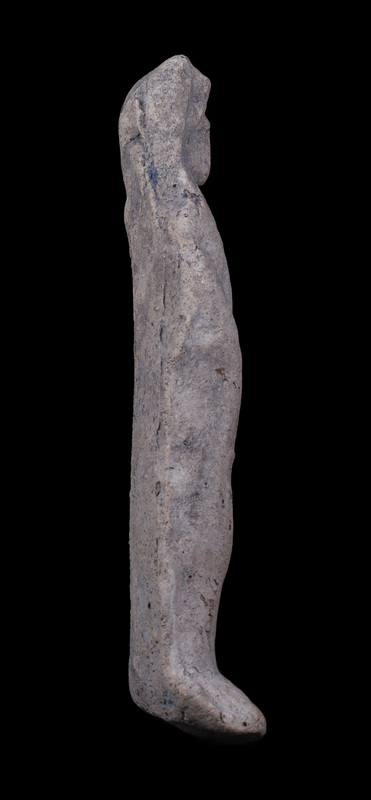 Mouldmade standing figure  wearing small polos over which draped palla which falls down along shoulders and is probably pulled  across front of body over slightly bent right arm; apparently palla held at left side at front of body by raised left hand, fingers of which crudely articulated.  Beneath polos hairline articulated and front of face crudely pinched forward; feet rest on shallow base which is bent up from the back and is not level, so that the figure cannot stand unsupported