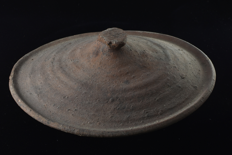 Convex lid with thickened edge and prominent wheel marks; in center of top a deformed short cylindrical handle which shows on surface striations of surface on which lid left to dry.