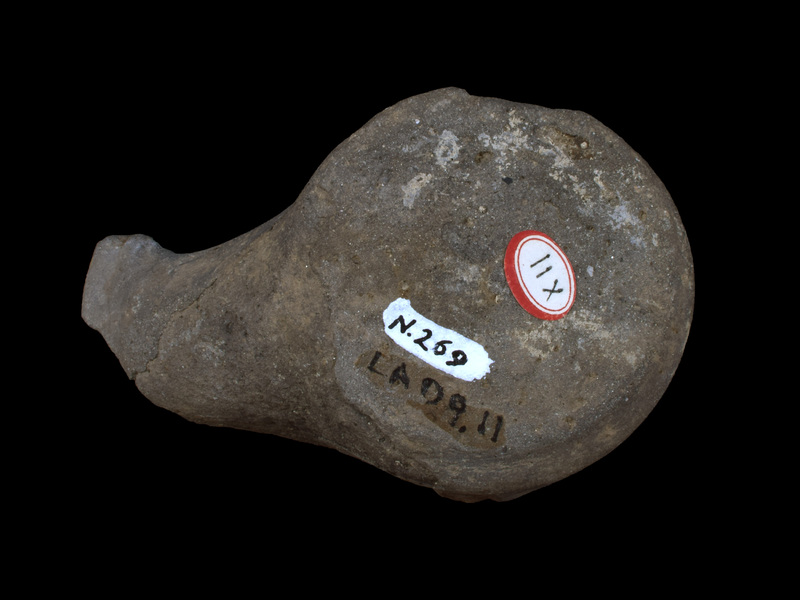 Tall, straight-sided reservoir w short bevel to ca. flat base; traces of small, un-pierced lug on edge of body wall and top surface which, as pres., plain & concave; broad, spathate nozzle.  No evidence of paint.
