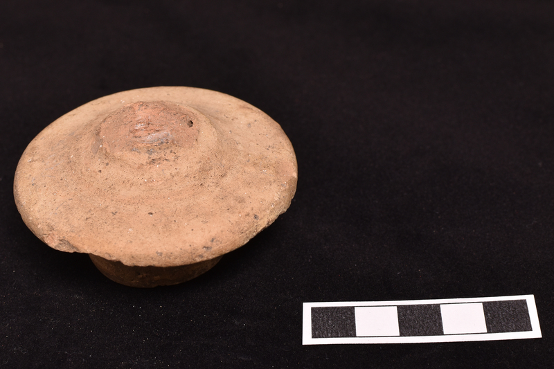Amphora stopper with exterior surface fairly flat in outer half rising to handle in central section; underside flat with prominent wheel marks and central projection in form of small thick walled bowl with deep hole in center extending into handle.