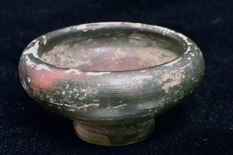 Bowl w shallowly convex sides spreading fr ring base, w shallow, concave nippled underside, to rounded shoulder with thick plain rim.  Coated all over int and ext w dark paint which ran onto underside of base.