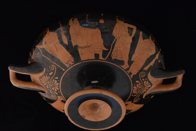 Kylix by Sabouroff Ptr, v. Oakley letter in file.  Decorated w scenes fr palaestra w  palmettes under handles; interior of handles & adjacent body, edge of foot & int of stem reserved. Tondo defined by discontinuous maeander w reserved exerque: Youth at l seated on altar facing r, swathed in himation which pulled over head on which added red fillet; at r standing youth in 3/4 view fr rear, r hand on hip, leans toward first, resting on smooth staff under l arm; wreath in added red.  Side A: Presentation of fillet to lyre-player; fr l to r: youth w fillet in added red in himation leaning r w staff under l arm & holding fillet in added red toward lyre-player swathed in himation, who sits on altar facing r holding lyre upright and wreath in added red; to r of lyre player frontal youth in himation pulled over l shoulder leaving chest bare,  r arm bent w hand on hip and w staff under l arm, face in profile to l, wreath in added red, feet crossed at ankles; at l another youth in himation, 3/4 view fr back, leaning in on staff under l arm  toward center, w r arm bent & hand on hip, face in profile to l w wreath roughly incised, possible modern;  on background aryballoi, strigils and one wooden cross; K A L O S in added red between figures 1 and 4.  Side B: Four youths in conversation fr l to r: frontal youth holding staff w curved top in r hand, r arm bent under himation, face in profile to r, wreath in added red; youth swathed in himation seated on altar facing r w arms bent holding bent r knee, all under himation; youth in 3/4 view fr rear leaning l w arm bent & hand on hip, leaning on staff under l arm, face in profile to l, fillet in added red; frontal youth with arms swathed in himation, r raised, left bent to hip, face in profile to l; on backgrd aryballoi, flute cases, strigils.