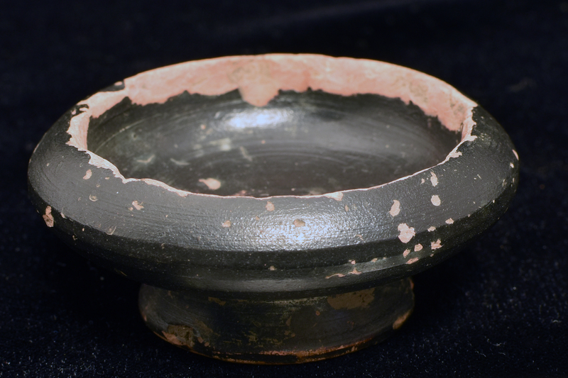 Squat carinated bowl on pedestal foot deeply concave on underside, in center of which low nipple, and in mid-wall incised line/wheel mark.  Ext and int coated w thick glaze/paint which splashed on underside of foot.
