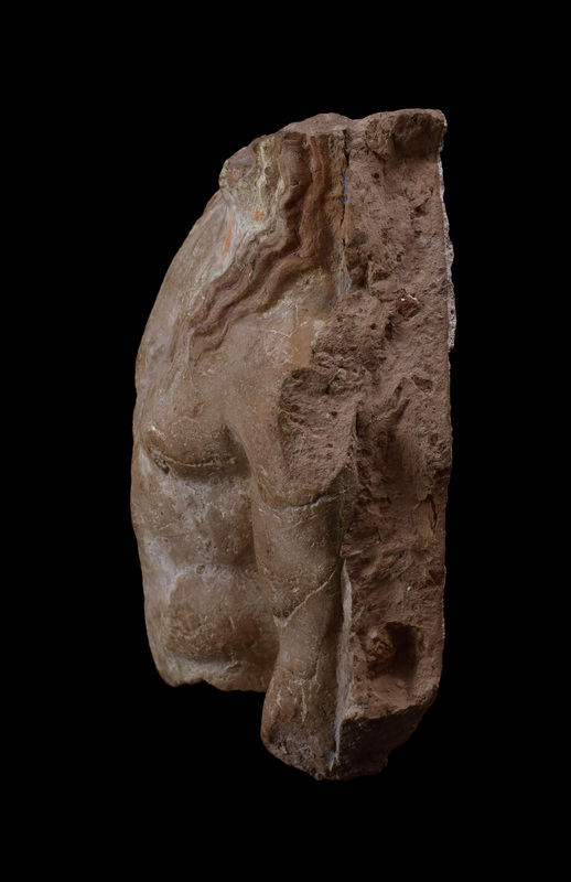 Terracotta slab w richly-modeled nude male torso, probably Apollo or Dionysus, w three tendrils of wavy hair falling over each shoulder, r arm held closer to body than l. Coated w white slip w hair painted red and background blue.  