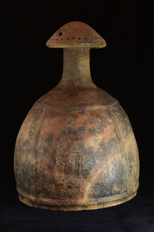 Imitation in clay of bronze helmet.  Rounded body rising from top of which tall, very slightly tapering cylindrical neck w finial in form of gabled roof which perforated horizontally under gable and by row of small holes around circumference of edge.  Body below neck & just above base set off by horizontal rib above & below and space between ribs divided into 4 sections by single vertical raised ribs.  Surfaces & ribs decorated with fine incision: on neck concentric horizontal lines, on shoulder pendant triangles below which isolated multiple zigzag devices, within ribbed sections metopes decorated with geometric patterns & surrounded by border of multiple zigzag devices; widely spaced groups of incised lines running across roof. Burnished surface.