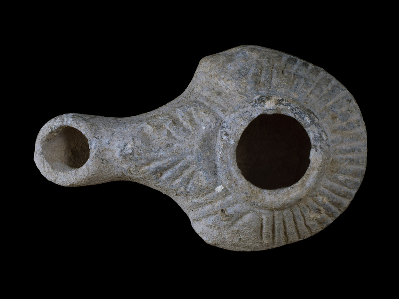 Handleless, carinated reservoir on low raised base; large fill hole w torus moulding border from which lines radiate out to carination; large palmette from torus over nozzle surface; incipient lugs, with relief ?eyes at carination on either side of base of nozzle.  Probably originally painted all over ext.