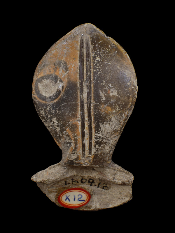 Fat leaf-shaped finial with two deep incised lines from base to tip attached to horizontally perforated, vertical loop handle.  On back on either side of handle relief potter's marks: V and reverse P.  Coated all over w dark paint, which owing to position in kiln, what looks like dark dot in center of one half of front surface in area mottled light in firing.