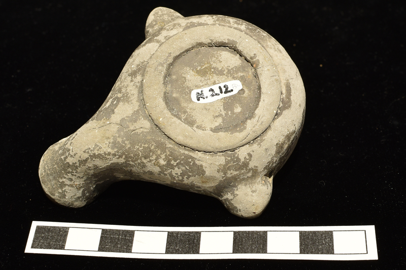 Squat, well-rounded reservoir on low ring base w flat discus w broad raised band around fill hole, narrower & higher band at edge, leaf-shaped lugs w traces of relief decoration, small ?loop handle & squat nozzle.  Relief decoration on rim band of large outline ivy leaves separated by small round clusters of grapes & at base of nozzle satyr head.  All of ext coated w now dark paint.