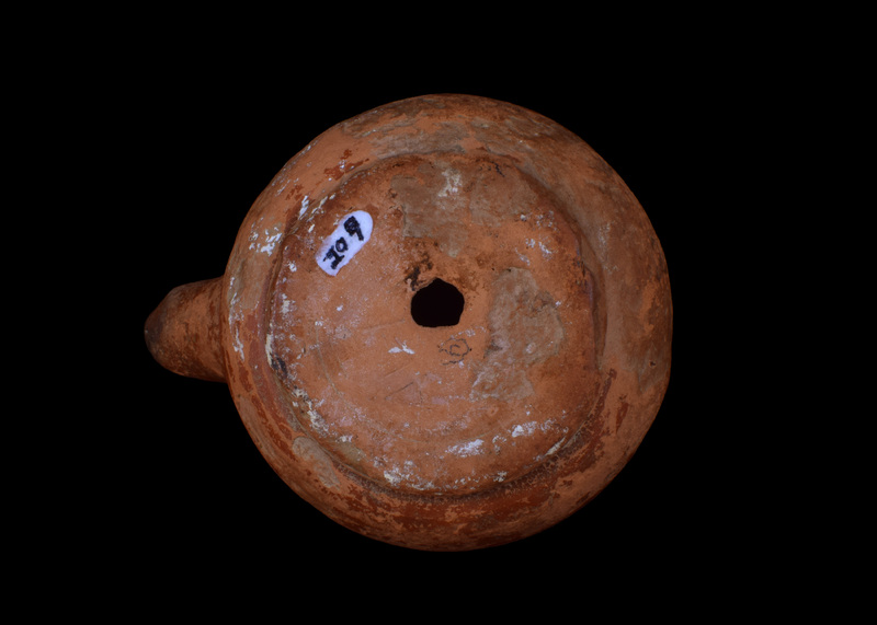 Squat round-carinated body on sharply defined offset base; shallowly concave discus w finely incised line defining it on ext, pairs of similar incised lines on body at mid-nozzle & at base of nozzle.  Opposite nozzle on shoulder horizontal volute handle.  Coated on ext w glossy red slip which darkened at edge of nozzle.  Scratched in base uppercase Alpha,  Gamma, Iota.