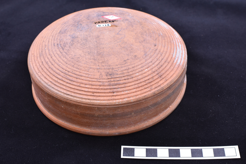 Low open bowl with straight sides and rolled rim, prominent wheel marks on interior walls; shallowly convex base with fine ribbing on outer half.  Painted stripe on exterior rim and just above base on exterior walls.