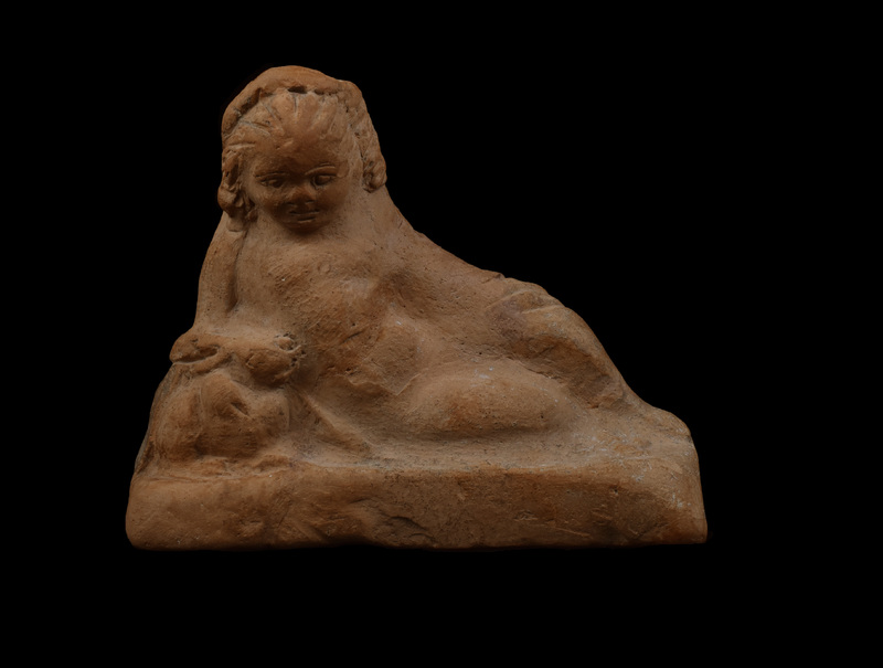 On rectangular base chubby Eros reclining on right elbow with right hand on rabbit.  Round face with eyebrows, eyes, nostrils, mouth, and cleft in chin articulated by incision; wreath on head with hair articulated by incisions going from forehead down back of head on either side of wreath, with clumps of hair articulated by irregular incision falling on either side of head.  Left arm covered by drapery stretched out and resting on bent left leg; incised lines roughly articulating folds of drapery; some articulation of feathers of left wing.  Raised band runs around back of figure under back of wings, possibly meant as drapery.