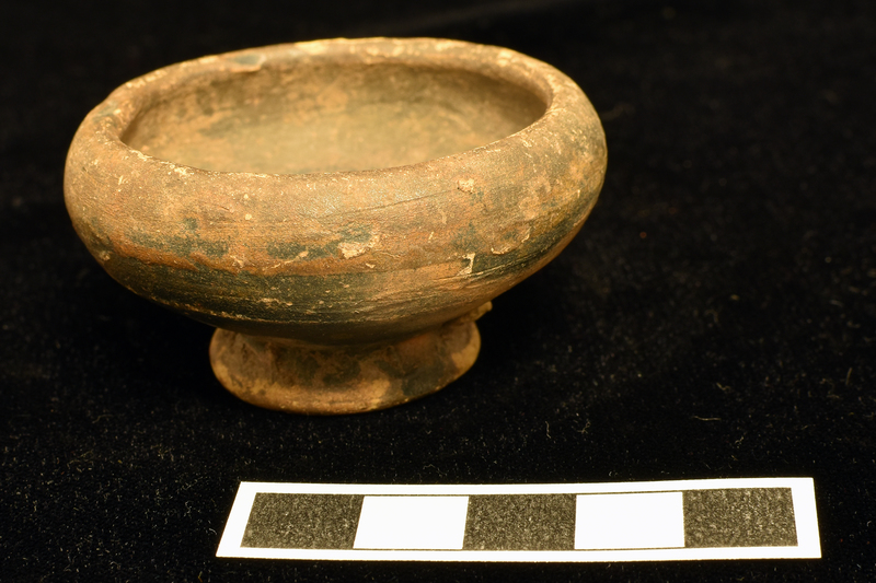 Bowl shallowly convex in lower half, curving more prominently above to rim; ring base w deeply concave, nippled underside. Staple-shape d pre-firing,  ?incision near rim on ext. Coated over all of int., most of ext w dark paint, underside of base only partially coated.