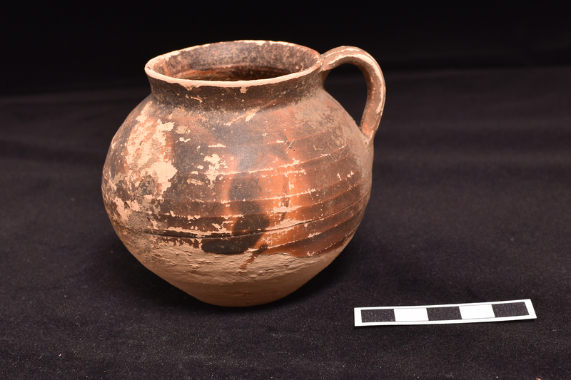 Globular body w flat base and slightly outturned vertical rim, prominent wheel marks on body; loop handle of flat plano-convex section , w two vertical grooves, attached from max D to rim.  Upper 2/3, including handle coated with dark brown paint w drips on lower body.