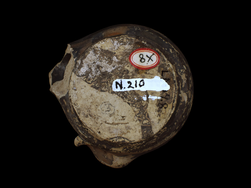 Handleless reservoir w almost straight sides rising from carination just above ring base; almost flat discus w large fill hole surrounded by two raised ridges of metal prototype; dolphin lug at one side.  Sides, discus, nozzle & dolphin coated w now dull, dark metallic paint which also on parts of int & base.