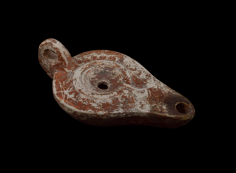 Convex sided reservoir curving in more strongly to discus which has flat rim decorated with shallowly-impressed ovolo pattern which extends outward from raised rim around concave center with fill hole; extending from rim on to nozzle relief spathate device; high loop handle.  Covered all over with reddish brown paint, darkened around wick hole.