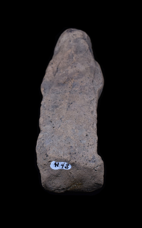 Mouldmade standing figure  wearing small polos over which draped palla which falls down along shoulders and is probably pulled  across front of body over slightly bent right arm; apparently palla held at left side at front of body by raised left hand, fingers of which crudely articulated.  Beneath polos hairline articulated and front of face crudely pinched forward; feet rest on shallow base which is bent up from the back and is not level, so that the figure cannot stand unsupported