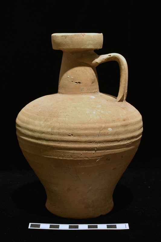 Piriform body with strong curve to very shallowly concave base slightly flattened along exterior edge; truncated conical neck flaring out at top to tall vertical rim which is concave on interior; flat handle with two broad grooves on exterior attached at top of neck and center of shoulder.  Body ribbed from base of shoulder to just above base with grooves broadening from top to bottom.