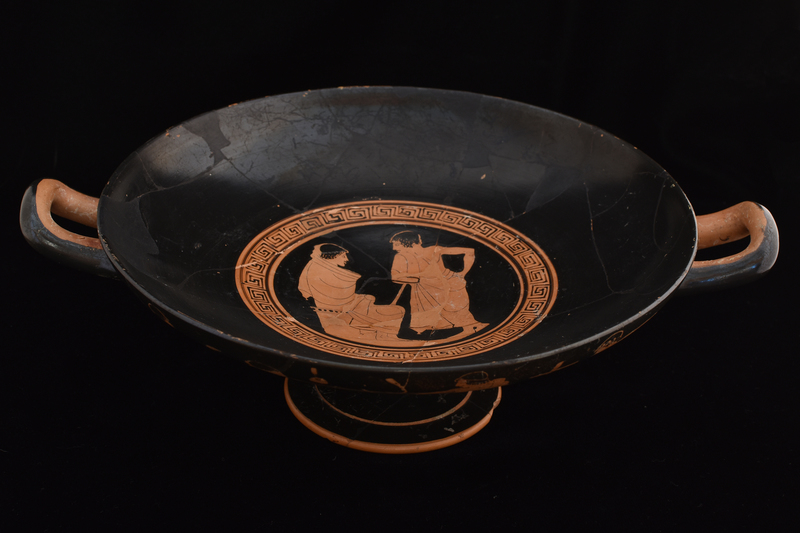 Kylix by Sabouroff Ptr, v. Oakley letter in file.  Decorated w scenes fr palaestra w  palmettes under handles; interior of handles & adjacent body, edge of foot & int of stem reserved. Tondo defined by discontinuous maeander w reserved exerque: Youth at l seated on altar facing r, swathed in himation which pulled over head on which added red fillet; at r standing youth in 3/4 view fr rear, r hand on hip, leans toward first, resting on smooth staff under l arm; wreath in added red.  Side A: Presentation of fillet to lyre-player; fr l to r: youth w fillet in added red in himation leaning r w staff under l arm & holding fillet in added red toward lyre-player swathed in himation, who sits on altar facing r holding lyre upright and wreath in added red; to r of lyre player frontal youth in himation pulled over l shoulder leaving chest bare,  r arm bent w hand on hip and w staff under l arm, face in profile to l, wreath in added red, feet crossed at ankles; at l another youth in himation, 3/4 view fr back, leaning in on staff under l arm  toward center, w r arm bent & hand on hip, face in profile to l w wreath roughly incised, possible modern;  on background aryballoi, strigils and one wooden cross; K A L O S in added red between figures 1 and 4.  Side B: Four youths in conversation fr l to r: frontal youth holding staff w curved top in r hand, r arm bent under himation, face in profile to r, wreath in added red; youth swathed in himation seated on altar facing r w arms bent holding bent r knee, all under himation; youth in 3/4 view fr rear leaning l w arm bent & hand on hip, leaning on staff under l arm, face in profile to l, fillet in added red; frontal youth with arms swathed in himation, r raised, left bent to hip, face in profile to l; on backgrd aryballoi, flute cases, strigils.