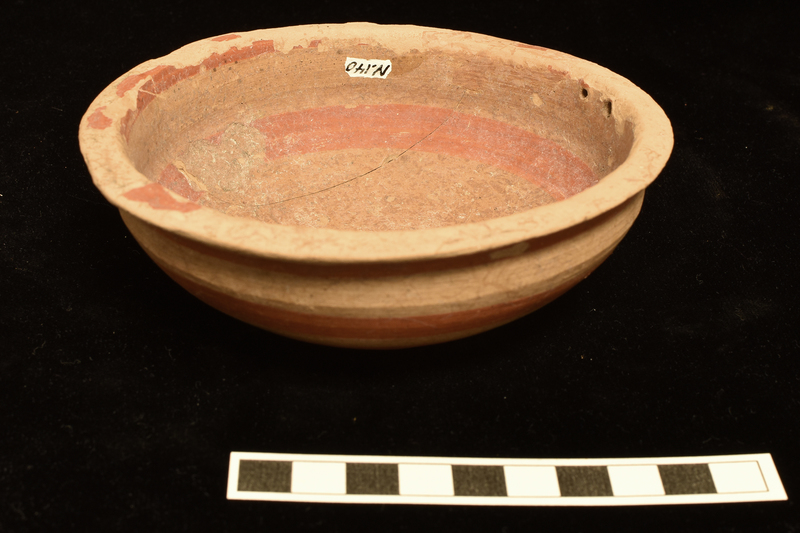 Shallow bowl with convex sides rising to poorly articulated carination and continuing  vertically to sharply outturned rim; low off-set base shallowly concave on underside.  Decorated interior and exterior with broad stripes in orange paint: int, solidly painted circle on base, single stripe about mid-body and narrow stripe on interior of rim which continues on to top and underside of rim: ext, 4 stripes from underside of rim to and including base, concentric swirl of paint on underside of base ending in irregular circle.  Two holes close to one another at juncture of rim and body.
