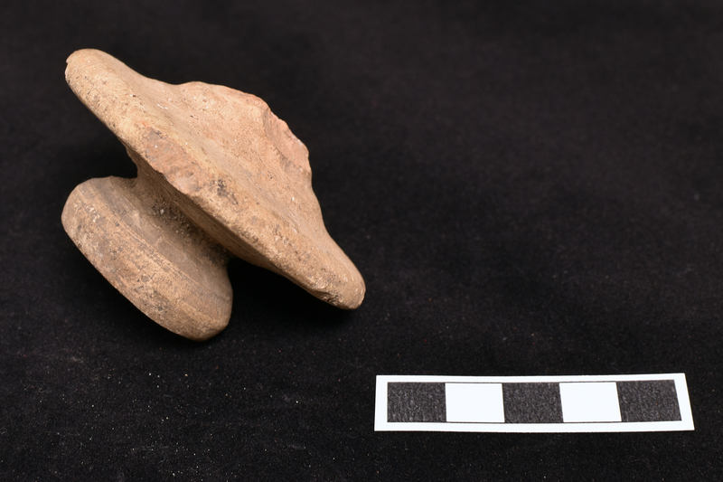 Amphora stopper with exterior surface fairly flat in outer half rising to handle in central section; underside flat with prominent wheel marks and central projection in form of small thick walled bowl with deep hole in center extending into handle.