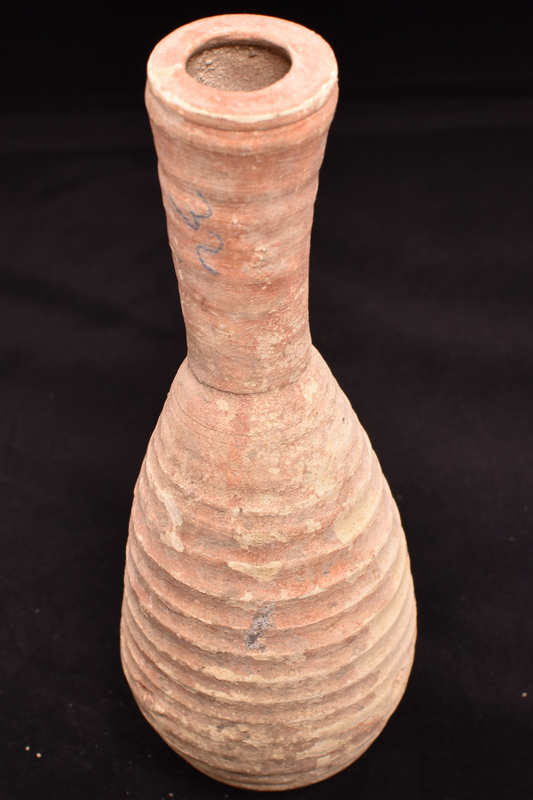 Elongated piriform body on small flat base; tall flaring neck with low discoid rim slightly smaller in D than top of neck; ribbed all over, shallow poorly articulated ribs on neck, broad, sharply articulated ribs on body.  Coated all over w red paint.