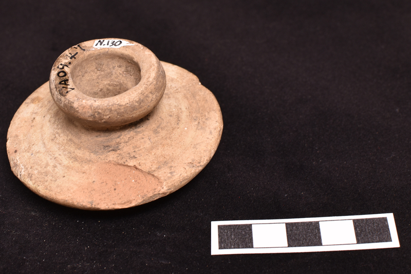 Amphora stopper with exterior surface fairly flat in outer half rising to handle in central section; underside flat with prominent wheel marks and central projection in form of small thick walled bowl with deep hole in center extending into handle.