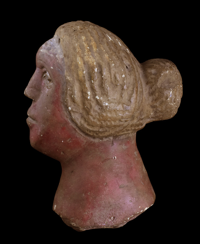 Head and neck of female with wig-like hair parted in middle and pulled back into a bun, hair strands marked by broad sawtooth impressions.  Flat oval face projecting forward with plastic eyes with pupils incised, prominent nose with nostrils indicated, and with horizontal mouth slit on raised surface indicating lips, upper lip with slight horizontal depression at center.  Thick neck spreading toward break, possibly not attached to a body but some kind of base.  Flesh painted reddish, hair showing traces of white paint which is better preserved on forehead in front of hair mass.